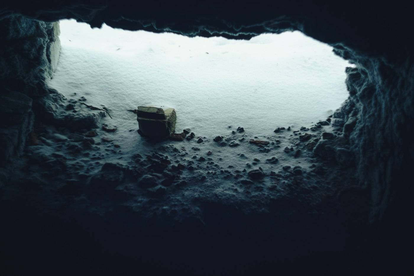 The view out of a dark cave towards a pale, snowy landscape