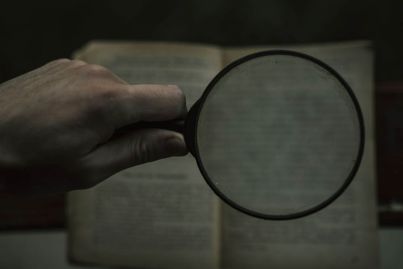 A hand holding a magnifying glass over an open book