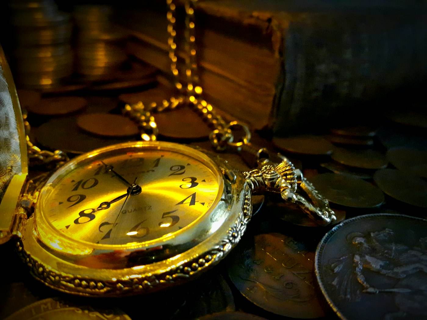 An antique pocket watch among old coins and books